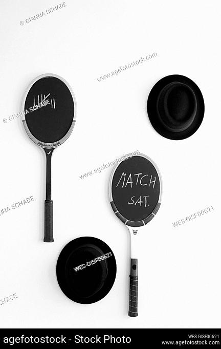 Black hats and blackboards made from tennis rackets hanging on white wall