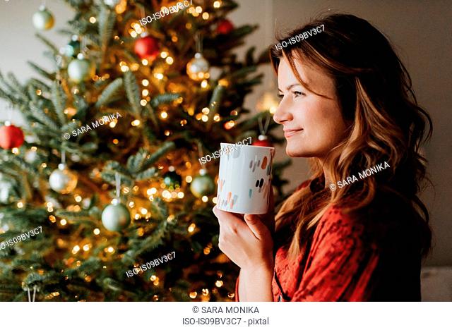Woman drinking coffee beside decorated Christmas tree