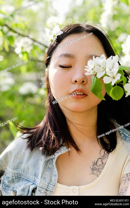Young woman with eyes closed by white flowers on branch