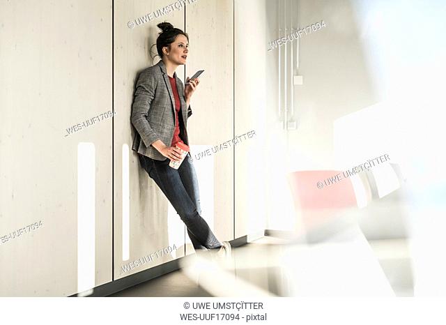 Businesswoman leaning against a wall in office using cell phone