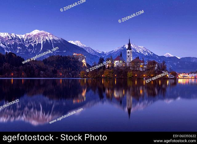 Scenic view of lake Bled at winter night with castle rock and St Martin church under beautiful starry sky reflected in lake water