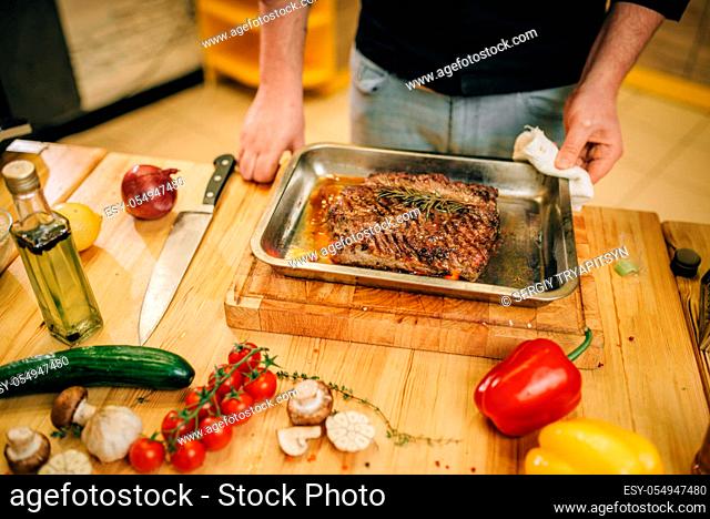 Male chef at the pan with roasted meat and vetables, kitchen on background. Man preparing beef on countertop