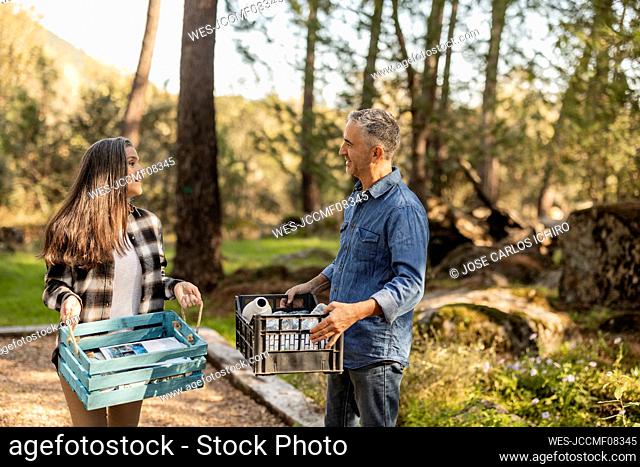 Man and woman carrying crates with separated waste standing in garden