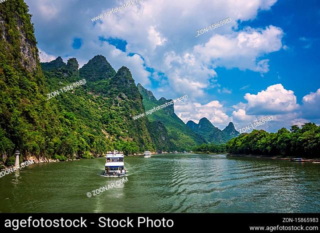 Yangshuo, China - August 2019 : Sightseeing boat carrying tourists sailing among stunning karst mountain scenery on the magnificent Li river between Guilin and...