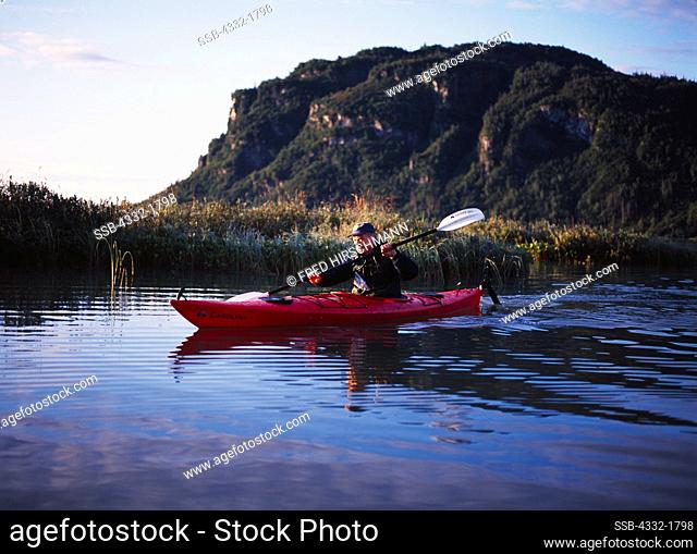 Carl Dixon paddling kayak in first light of sunrise, Big River Lakes, Redoubt Bay State Critical Habitat Area, Alaska