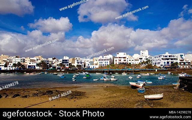 Canary Islands, Lanzarote, volcanic island, capital Arrecife, view over beach and harbor to part of Arrecife, boats in water, boats on land, sky blue
