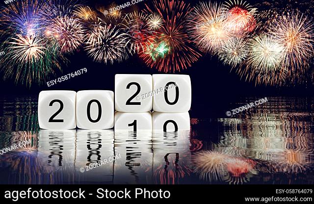 Composite of multiple firework explosions with calendar blocks showing 2019 sinking into the ocean as 2020 starts