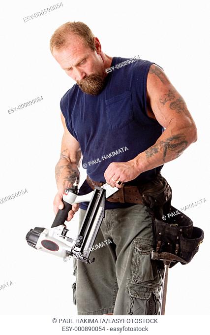 Strong man with tattoos loading a nail gun with nails, wearing a tool belt with hammer, isolated