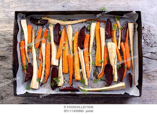 Roasted root vegetables and beetroot on a baking tray (seen from above)