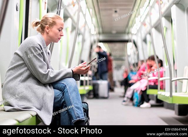 Portrait of lovely girl typing message on mobile phone in almost empty public subway train. Staying at home and social distncing recomented due to corona virus...