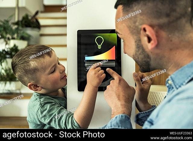 Boy adjusting lights on digital tablet with father at smart home