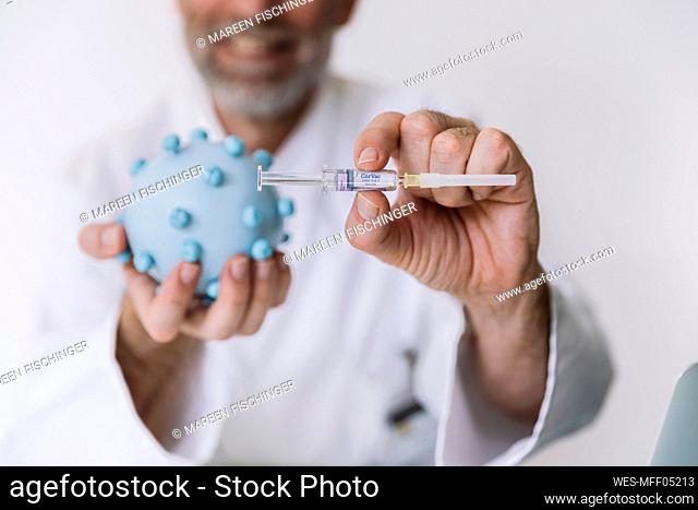 Scientist holding corona virus model and vaccine at desk