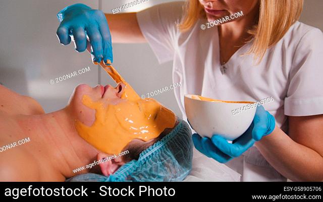 Close up of a person who visiting the beauty salon, fruit mask is applied on the face with a special wooden stick, beauty and self-care concept