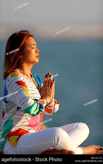 Woman practising yoga meditation by the sea before sunset as concept for silence and relaxation, United Arab Emirates, Middle East