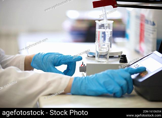 The hands of a technician in blue rubber gloves are holding a flask. Pharmaceutical industry. Chemical laboratory