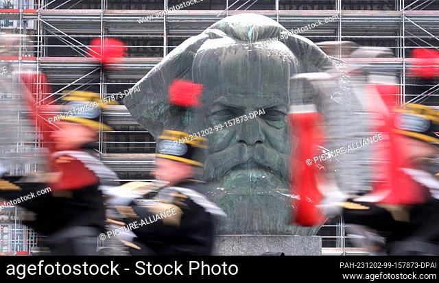 02 December 2023, Saxony, Chemnitz: Participants in a mining parade walk past the Karl Marx Monument. On the eve of the first Advent