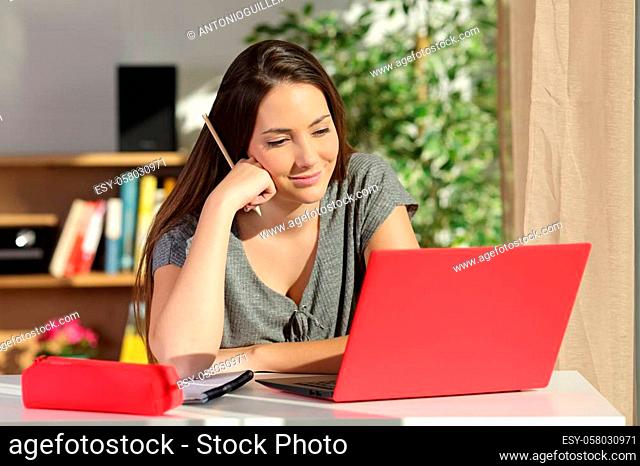 Studious student e-learning at home using a red laptop