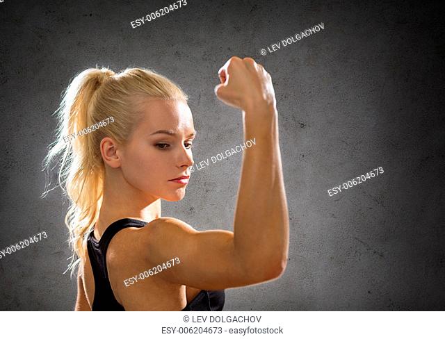 fitness, sport and strength concept - sporty woman flexing her biceps over concrete wall background