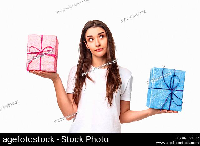 Celebration, holidays and presents concept. Portrait of thoughtful young girl taking decision, look up wondered, weighing gift boxes in hands spread sideways