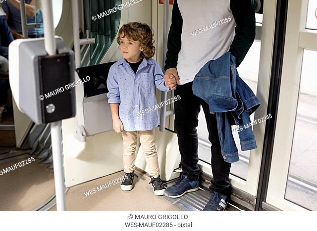 Father and son standing hand in hand in a tram