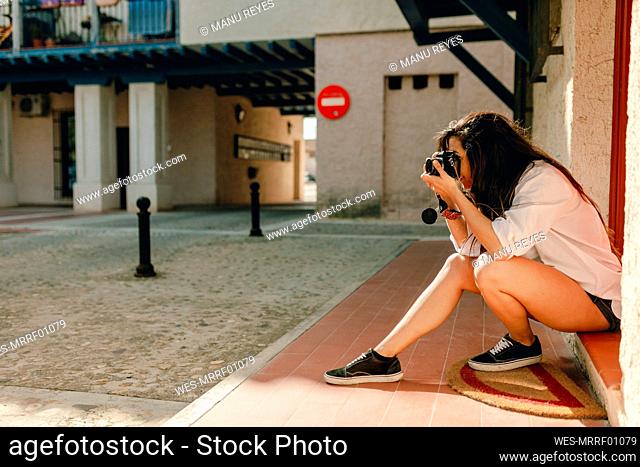 Woman taking photo through camera while sitting at footpath