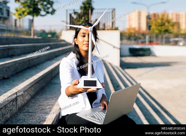 Woman with wind turbine model and laptop sitting on staircase