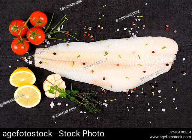 Fresh halibut fillet with fresh herbs and garlic on dark black stone background top view. Luxurious seafood eating background