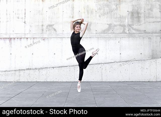 Ballerina in black leotard dancing in front of concrete wall