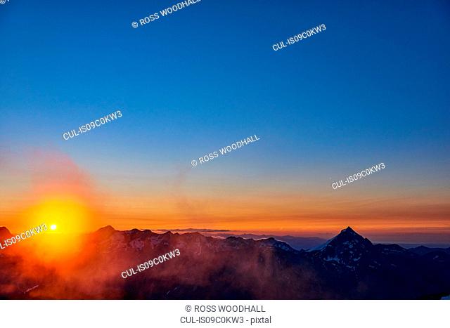 Sun glowing on horizon over mountain range, Saas-Fee, Valais, Switzerland