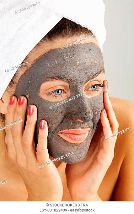 Beautiful woman with purifying facial mask keeping her palms by her face