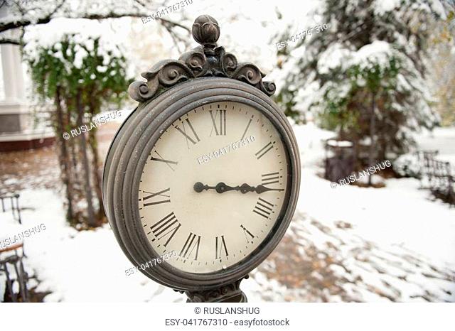 wrought-iron clock with roman numerals on the background of snowy street