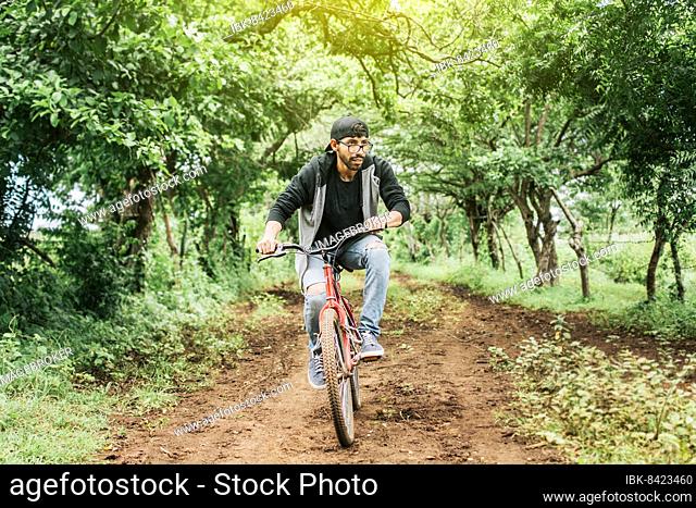 Teenage guy riding a bike in the countryside, Portrait of a guy in cap riding a bike on a country road, Person riding a bike in the countryside
