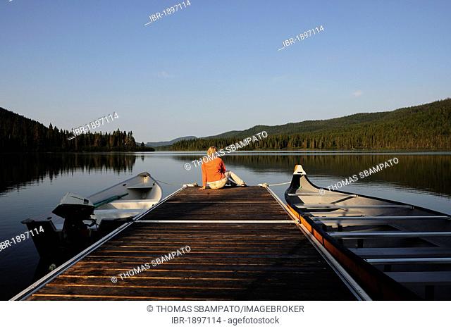 Woman sitting on a jetty overlooking a lake, Gaspésie National Park in the middle of the Chic-Choc Mountains, also known as Shick Shocks, Gaspe Peninsula