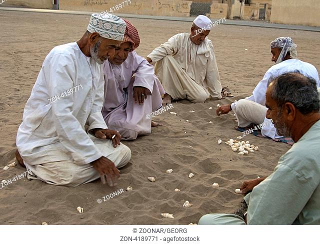 Eine Gruppe omanische Männer spielt Hawalis mit Muscheln im Sand, omanische Variante des Mancala-Spiels, Sultanat Oman / A group of Omani men playing Hawalis...
