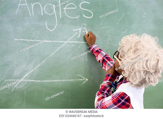 Schoolboy doing mathematics on chalkboard in classroom