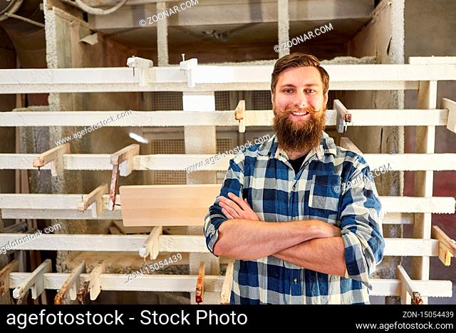 Selbstbewusster Hipster Möbelbauer vor der Verleimpresse in der Werkstatt