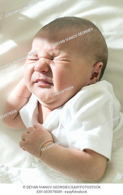 Unhappy frowning baby. White clothes
