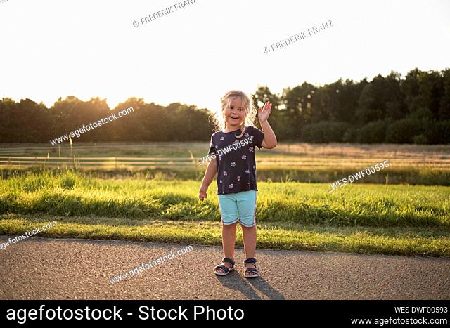 Happy cute girl waving standing on sunny day