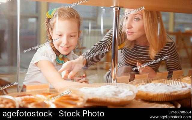 Girl with a pigtail and her mommy look at the pies in the window choosing, people on the other hand showcases