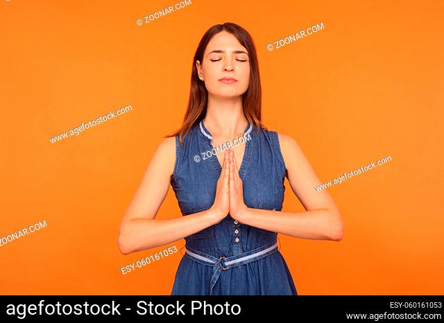 Mindfulness, zen practice. Happy calm brunette woman in denim dress doing yoga exercise with hands together, meditating, feeling tranquil relaxed
