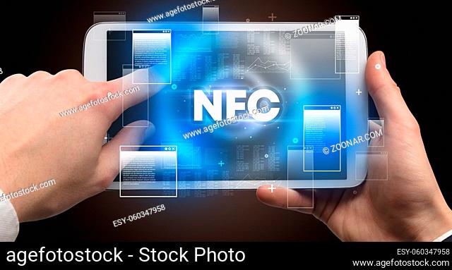 Close-up of a hand holding tablet with NFC abbreviation, modern technology concept