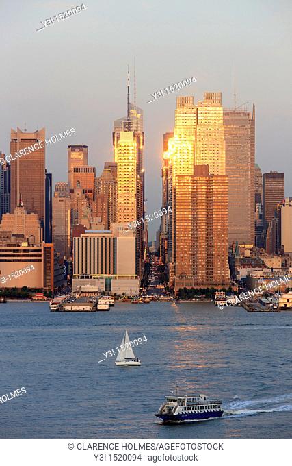 The setting sun reflects off the windows of Manhattan skyscrapers on 42nd street in New York City, New York, USA as viewed over the Hudson River from New Jersey