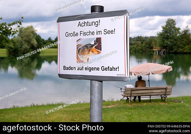 02 July 2020, Bavaria, Zolling: A sign with the inscription ""Attention! Big fish in the lake! - Swim at your own risk!"" is written on the bank of the Anglberg...