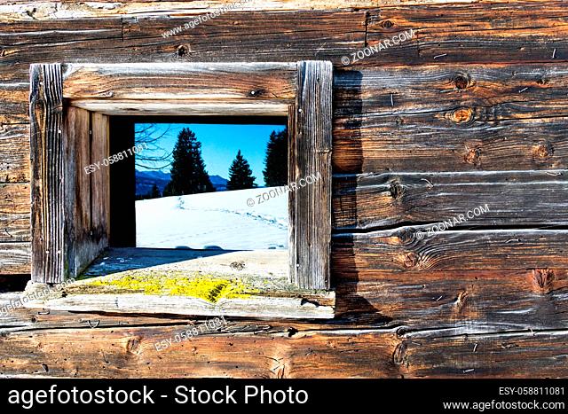 Vintage window of old wooden cabin mirrors winter landscape. Wooden rustic background. Reflections of trees and mountains in window glass