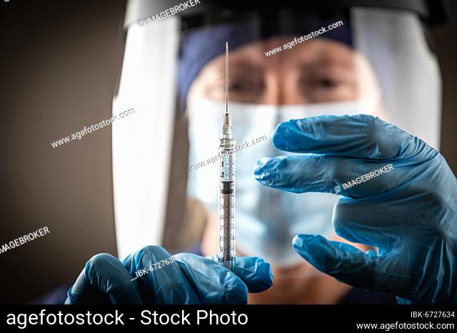 Doctor or nurse holding medical syringe with needle against dark background