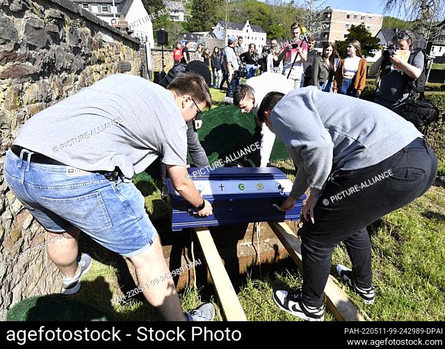 11 May 2022, North Rhine-Westphalia, Schleiden: Pupils of the Johannes-Sturmius-Gymnasium let the coffin with the bones of a school skeleton into the grave at...