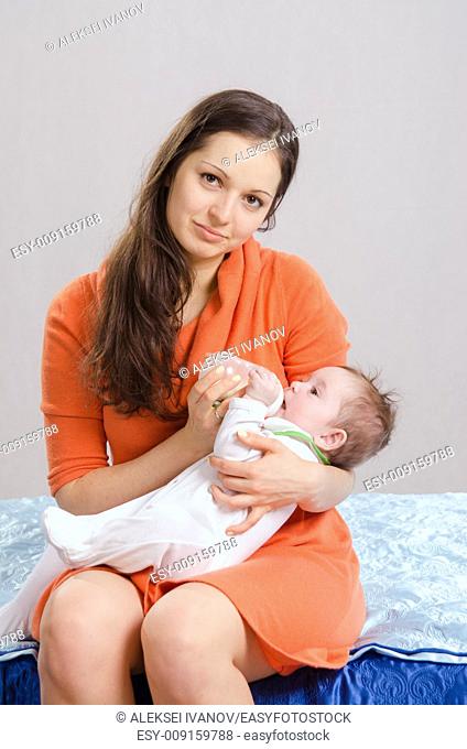 Six month old baby drinking milk from a bottle with a nipple, lying on his mother's arms