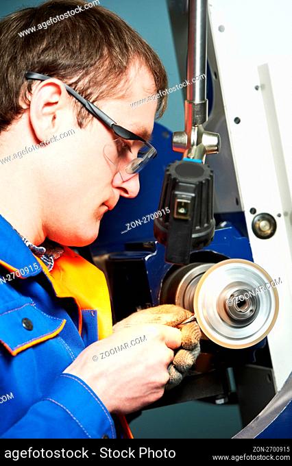 worker in uniform and protective glasses working on sharpening machine tool