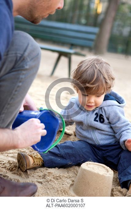 Toddler boy playing in sand with his father