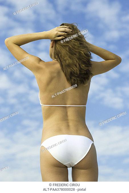 Woman in bikini standing with hands in hair, low angle rear view
